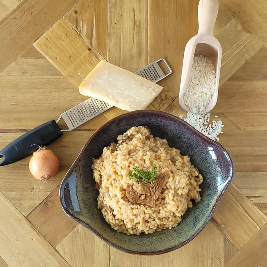 Braune Schalen mit Steinpilz-Risotto, Zwiebel, Reis und einem Stück Parmesan auf einem Holztisch