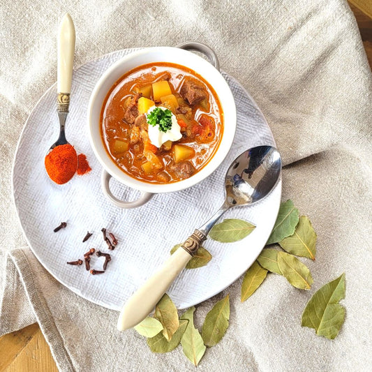 Gulaschsuppe in einer weissen Suppentasse und Gewürzen als Deko