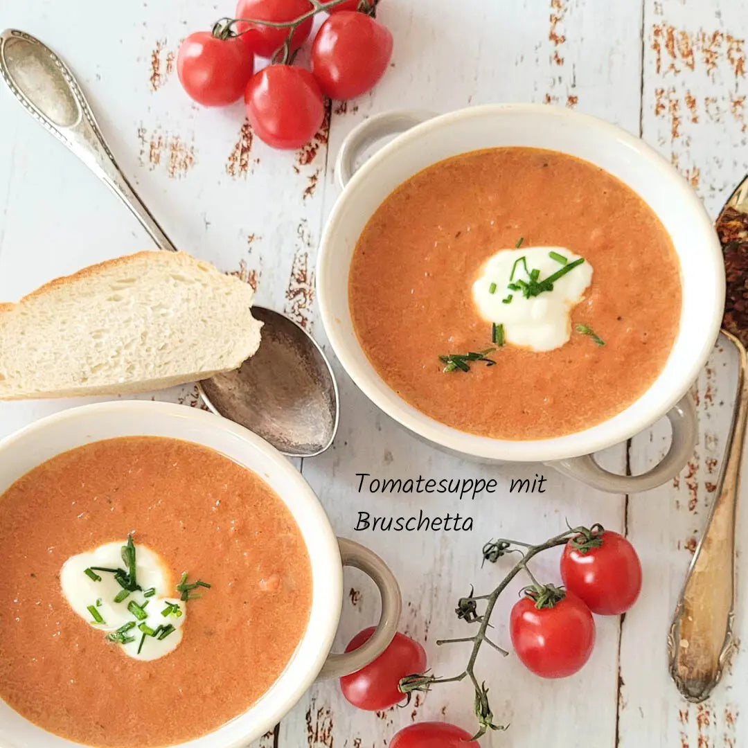 Cremige Tomatensuppe mit Bruschetta-Gewürz, frischen Tomaten und einem Topping aus Sauerrahm und Schnittlauch, serviert mit knusprigem Brot.