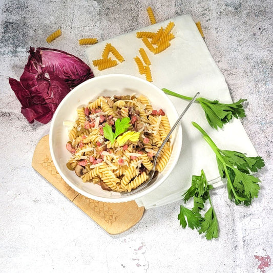 Eine weisse Schüssel mit Pasta, Radicchio und Bacon steht auf einem Holzbrett mit weisser Serviette