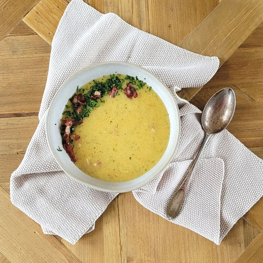 Auf dem Tisch eine helle Schale gefüllt mit Griesssuppe und Petersilien-Speck Garnitur. 