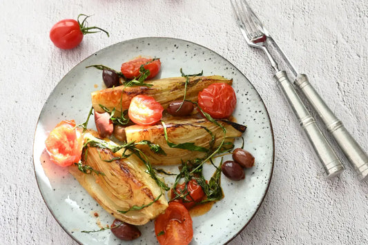Gebratener Fenchel, Kirschtomaten, Oliven und Rucola sind auf einem hellen, rustikalen Teller angerichtet.