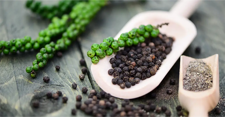 Auf Einem Rustikalen Brett Liegen zwei Holzschäufelchen mit gemahlenem, grünem und schwarzem Pfeffer